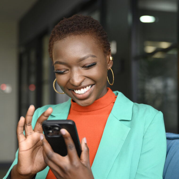 Femme souriante regardant son téléphone pour suivre le remboursement de ses soins depuis son compte ameli